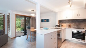 A modern kitchen with a central island, built-in oven, and a dining area with a table and chairs.