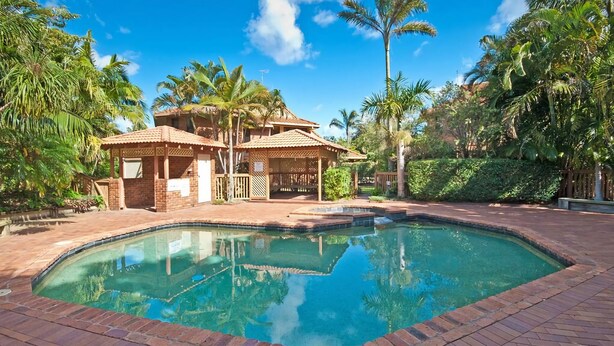 A pool area with a clear pool, a gazebo, and a building with a tiled roof.