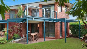 A two-story house with a covered patio area, a brick exterior, and a small garden.
