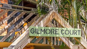 A wooden sign with the text "GILMORE COURT" mounted on a structure with a wooden lattice design.