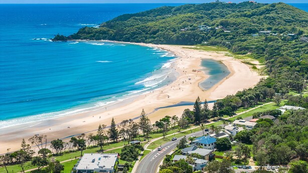 A coastal area with a beach, a road, and residential buildings.