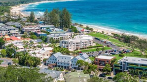 A coastal residential area with modern buildings, a beach, and a clear view of the ocean.