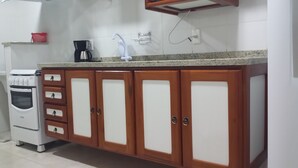 A kitchen with wooden cabinets, a white oven, a coffee maker, and a sink with a faucet. - Located 150 meters from the most charming beach in Arraial do Cabo, this 2-bedroom apartment features air conditioning! (Arraial do Cabo)
