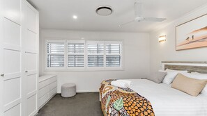 Une chambre à coucher comprenant un lit, une armoire, une fenêtre avec des stores, un ventilateur de plafond et un tableau accroché au mur.
