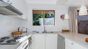 Ett modernt kök med vita skåp, en spis i rostfritt stål, en diskmaskin och ett fönster med utsikt över grönområden utanför.