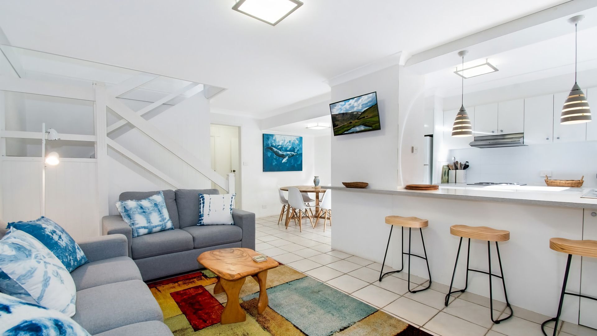 A modern apartment with a living room, dining area, kitchen, and a staircase.