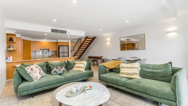 A modern living room with two green sofas, a marble coffee table, and a kitchen in the background. - Byron Bay Accom - Solace 1 - 8 Lawson Street (Byron Shire)