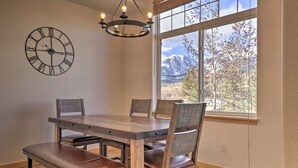 Ein Essbereich mit Holztisch und -stühlen, einer Wanduhr und einem großen Fenster mit Blick auf die Berge.