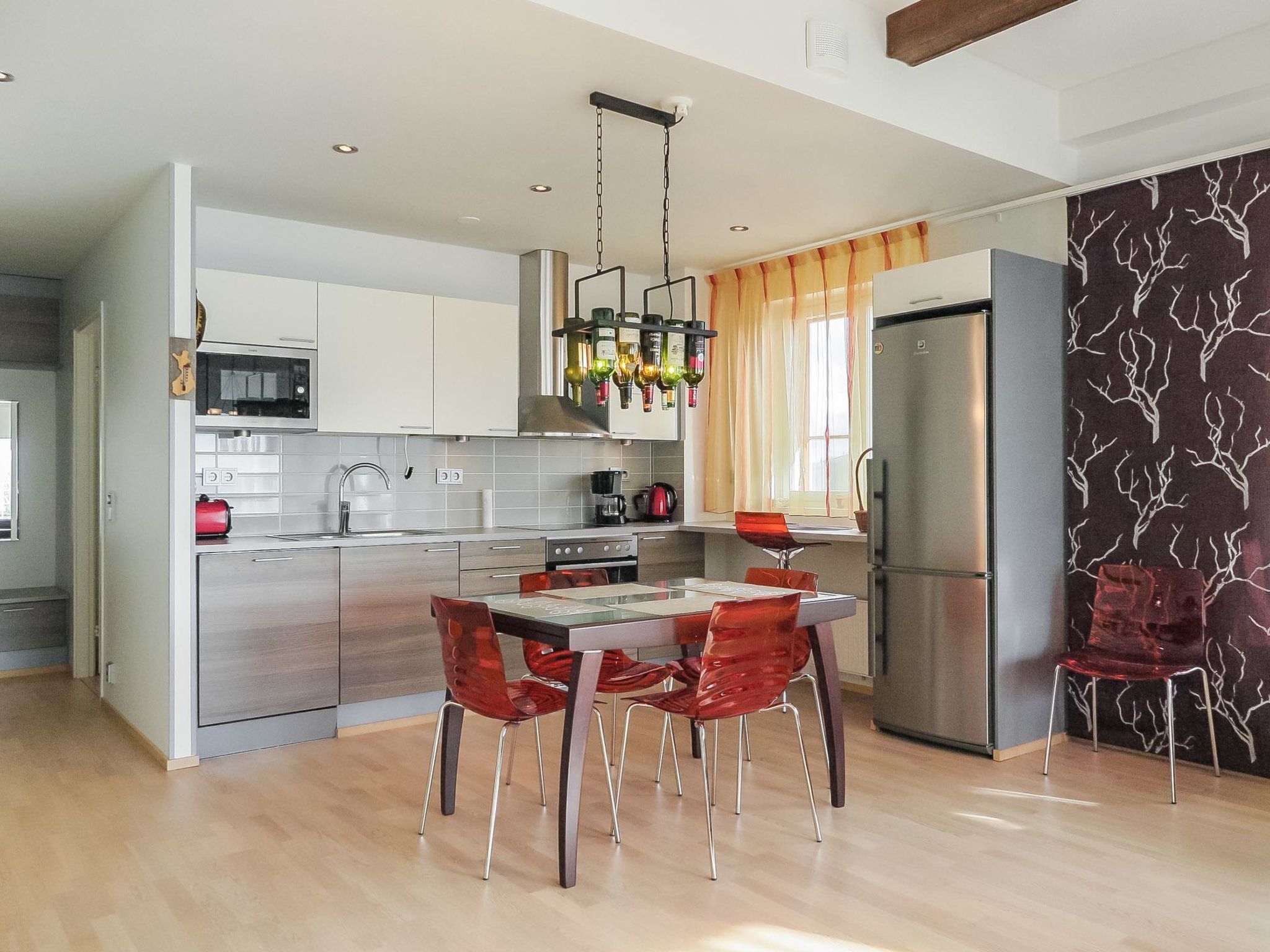 A modern kitchen with a dining area, featuring a stainless steel refrigerator, a microwave, and a hanging light fixture.