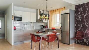 A modern kitchen with a dining area, featuring a stainless steel refrigerator, a microwave, and a hanging light fixture.