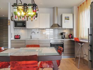 Una cocina moderna con comedor, electrodomésticos de acero inoxidable y una lámpara original hecha con botellas de vino.
