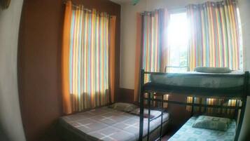 A dormitory room with bunk beds, striped curtains, and a ceiling fan.