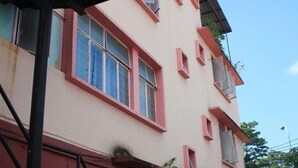 A multi-story building with a flat facade, multiple windows with red frames, and a visible balcony on the upper floor.