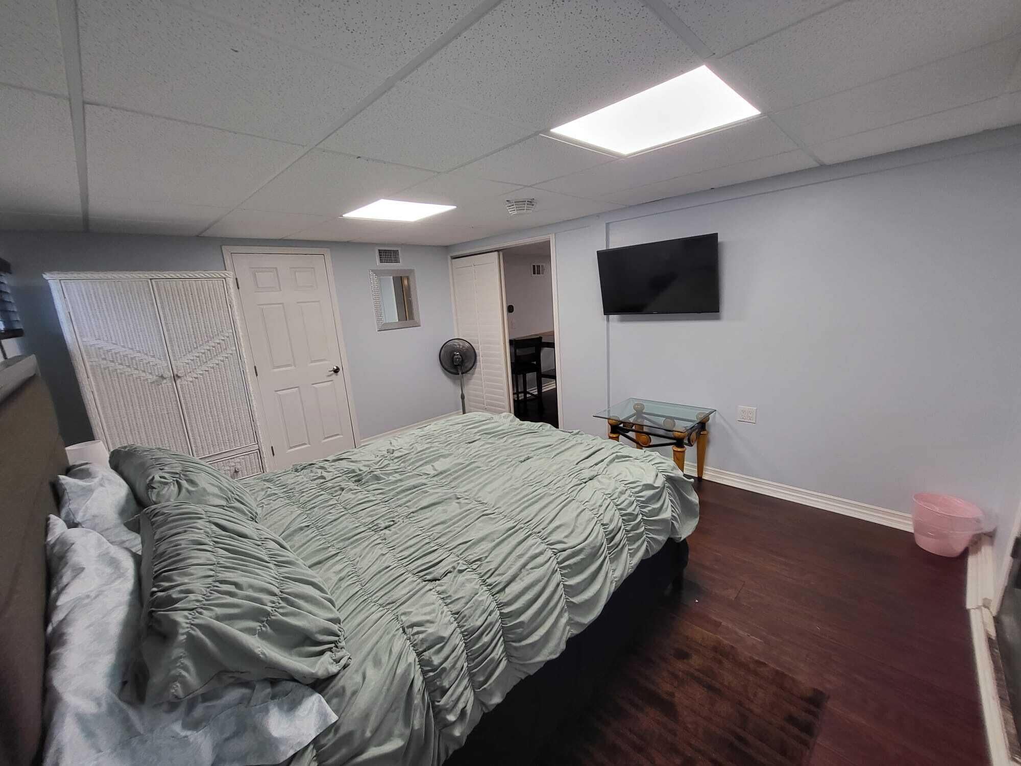 A bedroom with a bed, a TV, a fan, and a small table.