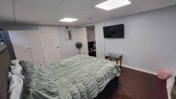 A bedroom with a bed, a TV, a fan, and a small table.
