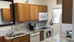 A compact kitchen with wooden cabinets, a microwave, a coffee maker, and a dishwasher.