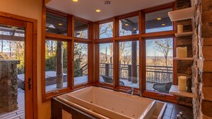 Une salle de bain avec une grande baignoire, des fenêtres en bois et un mur en pierre.