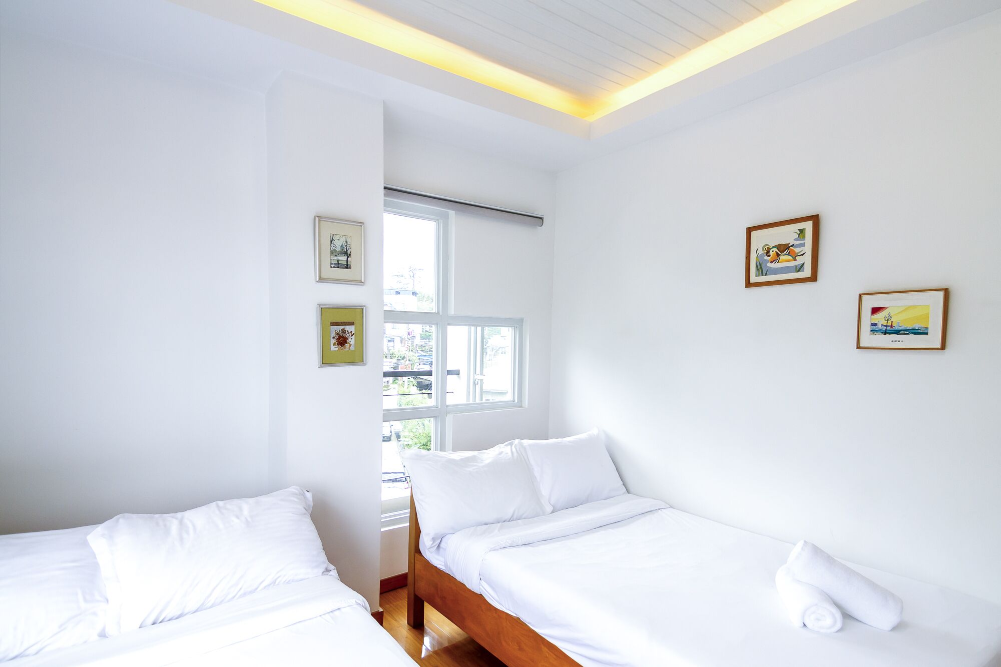 Una habitación con dos camas individuales, una ventana y cuadros en la pared.