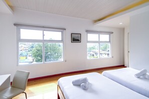 A hotel room with two beds, a chair, and large windows with a view of buildings and trees.
