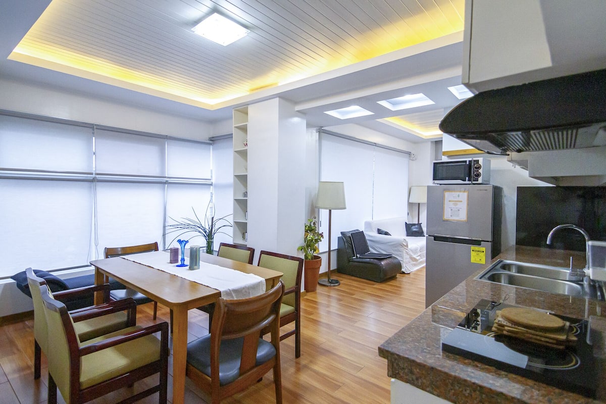 A hotel room with a dining area, kitchenette, and a bed.