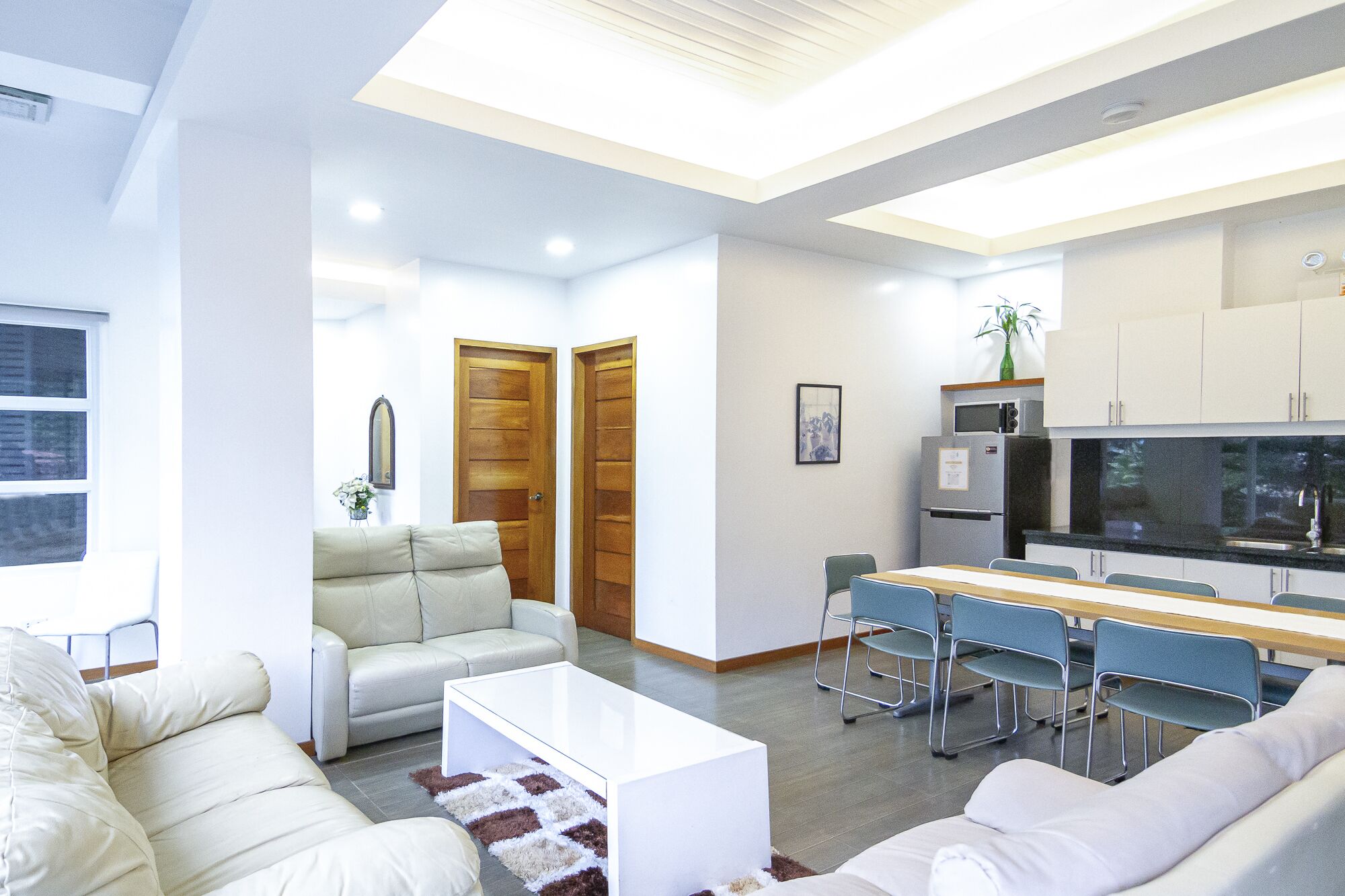 Un soggiorno moderno con un divano, un tavolino da caffè e una zona pranzo con sedie. Si nota anche una cucina con elettrodomestici e pensili.