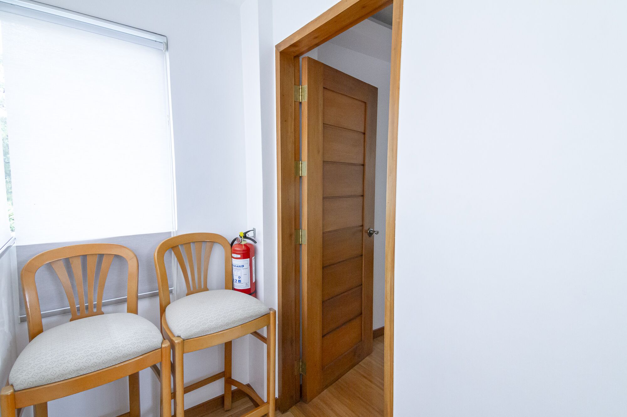 Una habitación con dos sillas de madera, un extintor y una puerta de madera.