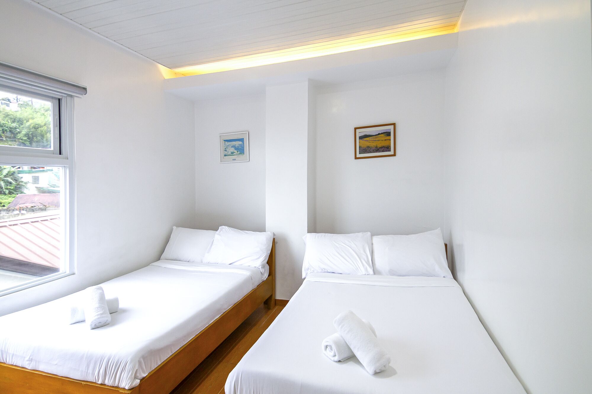 A hotel room with two single beds, white bedding, a small window, and a framed picture on the wall.