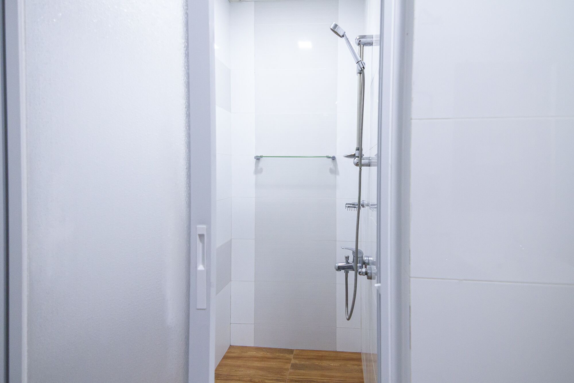 A narrow, tiled shower area with a wooden floor and a glass door.