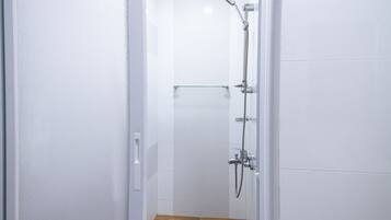 A narrow, tiled shower area with a wooden floor and a glass door.