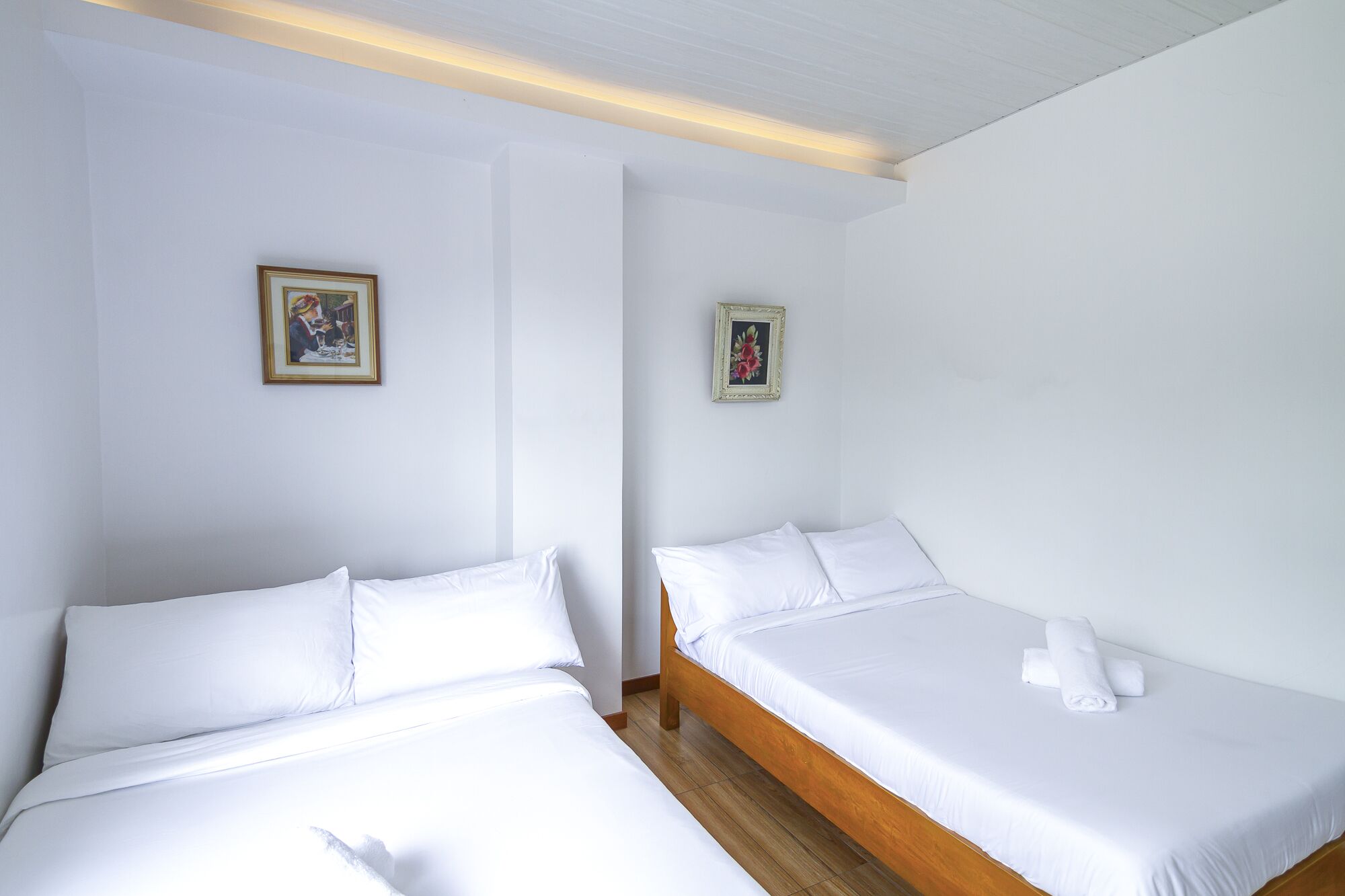 Habitación de hotel con dos camas individuales, ropa de cama blanca, cabeceros de madera y dos cuadros en las paredes.