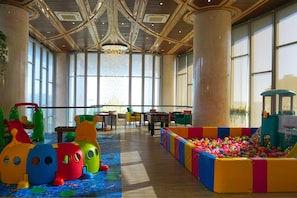 A spacious indoor play area with a ball pit, colorful play structures, and large windows allowing natural light.
