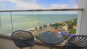 Un balcón con dos sillas y una mesa, con vistas a una playa y el océano, donde se ven barcos.