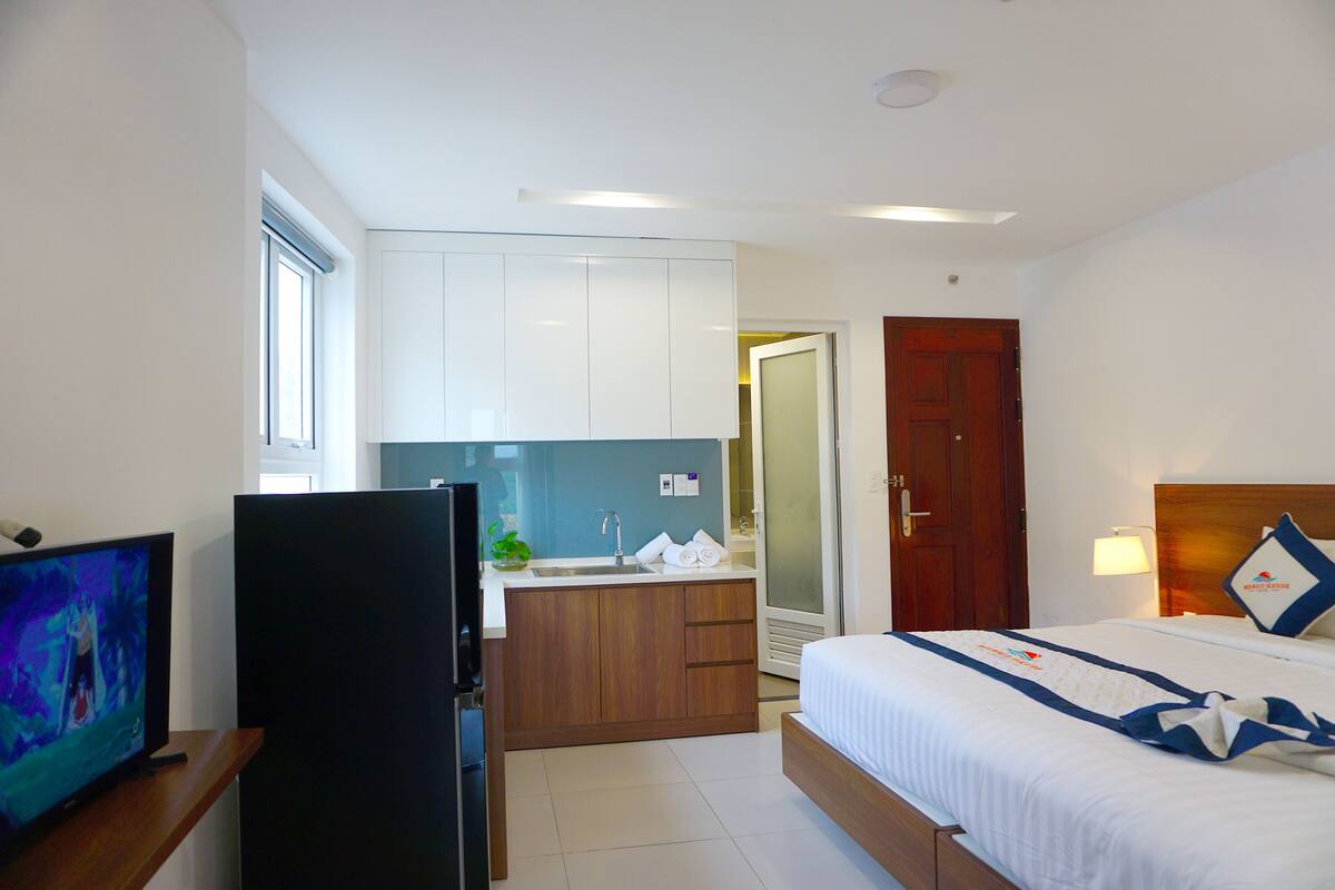 A hotel room with a bed, a TV, a kitchen area, and a door leading to another room.