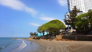 Un hotel frente a la playa con un gran árbol, playa de arena y vista al océano.
