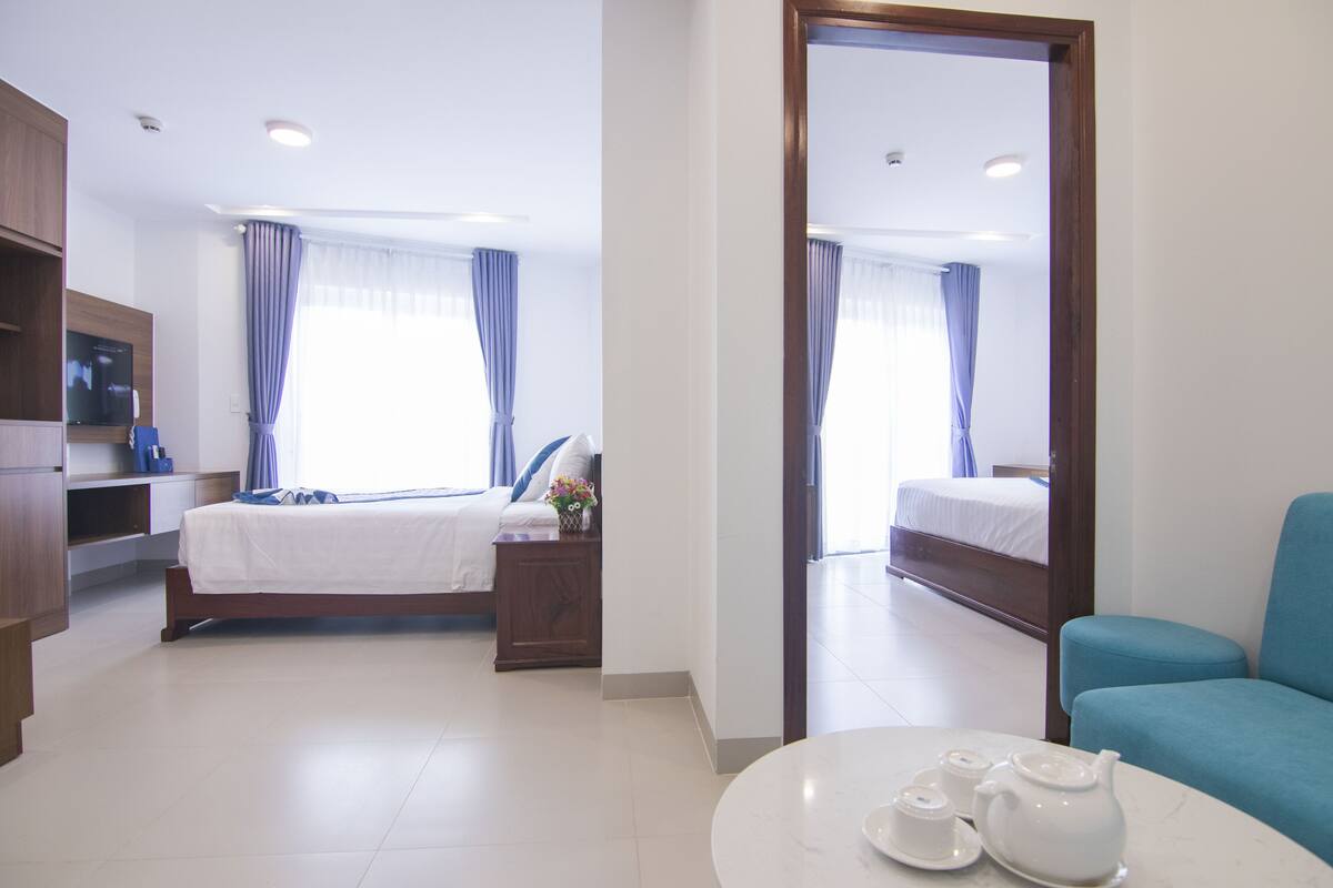 A hotel room with a bed, a desk with a computer, a table with a teapot and cups, and a mirror reflecting the room.
