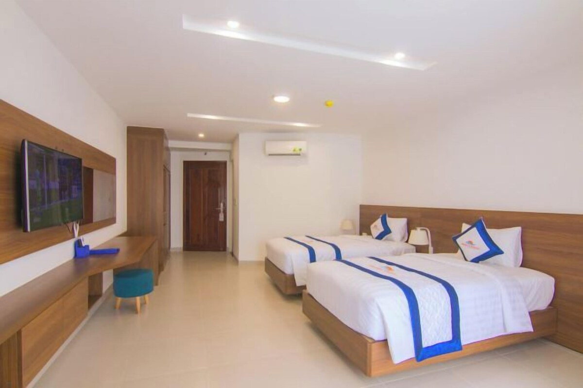A hotel room with two beds, a desk, a television, and a door leading to another room.