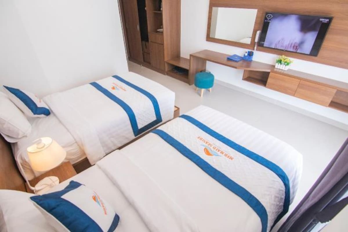 A hotel room with two beds, a TV, a desk, and a mirror.