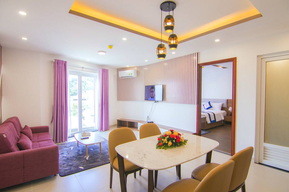 A modern hotel room with a sofa, dining table, and a bed.