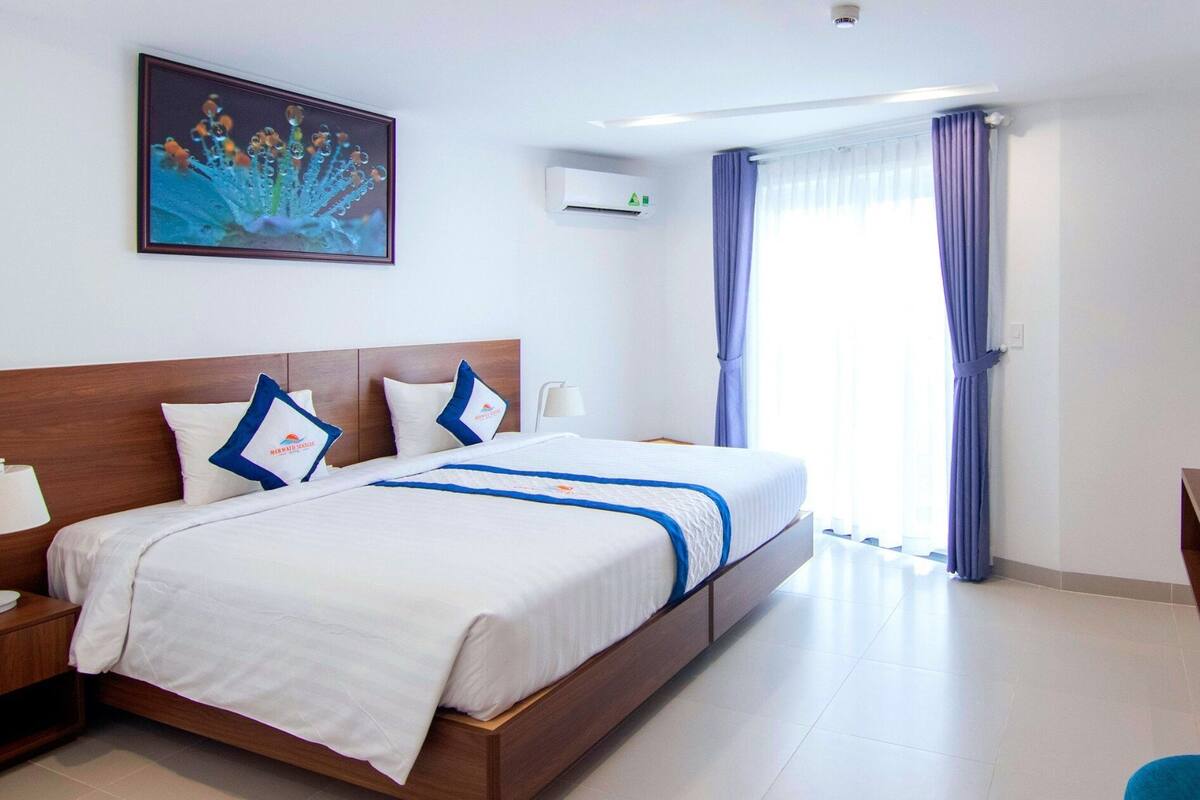 A hotel room with a bed, a desk, a television, and a window with curtains.