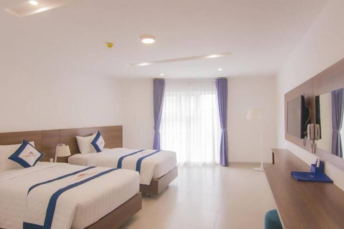 A hotel room with two beds, a desk, a mirror, and a TV.