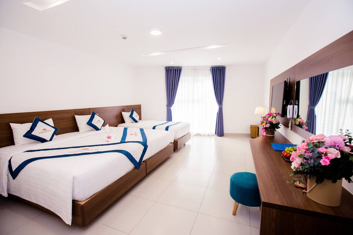 A hotel room with two beds, a wooden headboard, a desk with a vase of flowers, and a large mirror.
