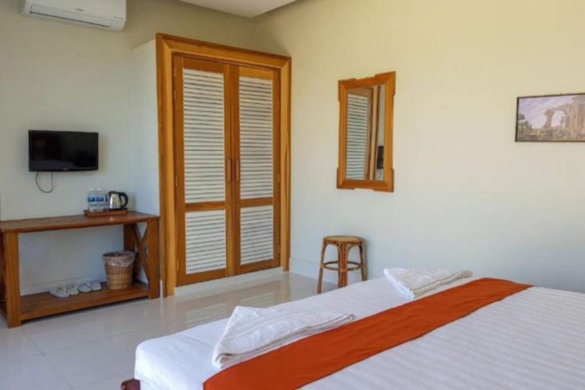 A hotel room with a bed, a TV, a desk with a coffee maker, a mirror, and a picture on the wall.