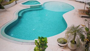 En pool med en usædvanlig form, omgivet af liggestole og potteplanter.