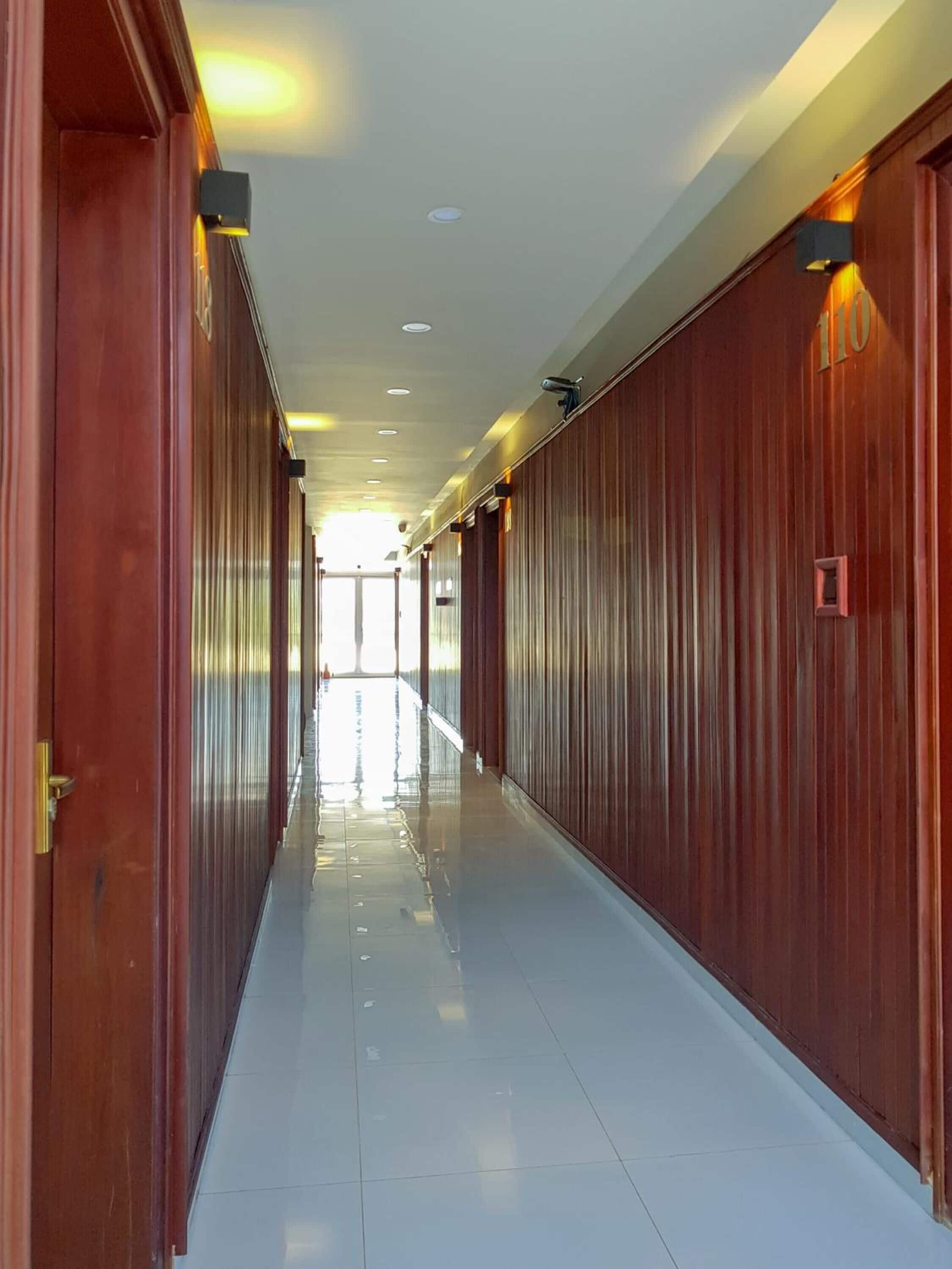 A long, narrow hallway with wooden paneling on both sides and a shiny tiled floor.