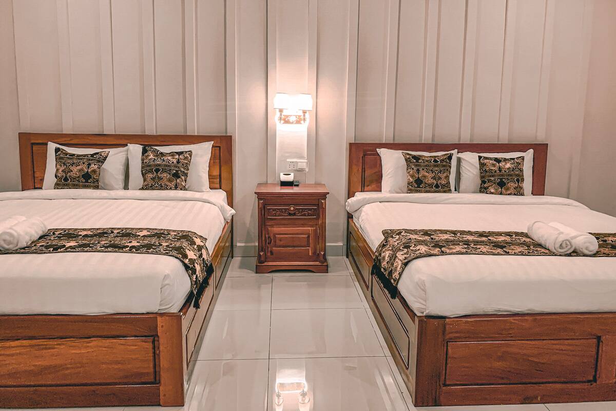 A hotel room with two wooden beds, white bedding, patterned throw blankets, a nightstand with a lamp, and a mirror.