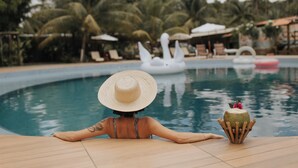 Une personne se détend au bord d’une piscine, avec des chaises longues et des parasols en arrière-plan.