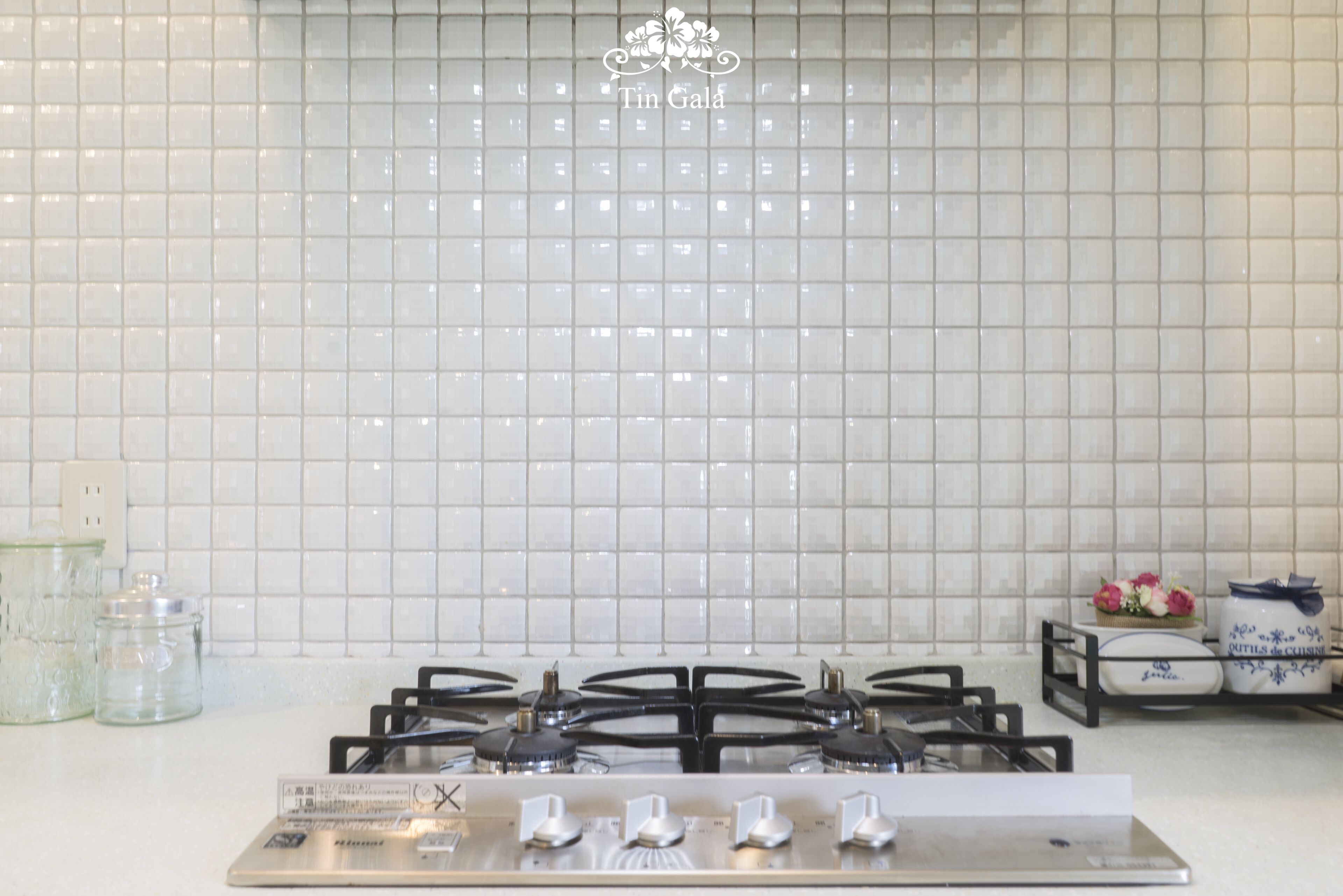 A kitchen with a gas stove, white tiled backsplash, and kitchenware on the counter.