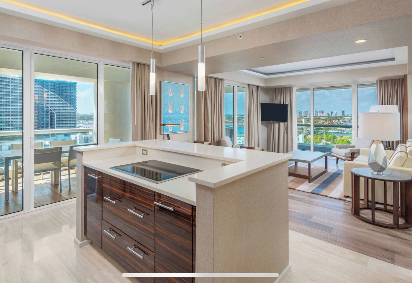 A modern hotel room with a kitchen island, large windows, a flat-screen TV, and a city view.