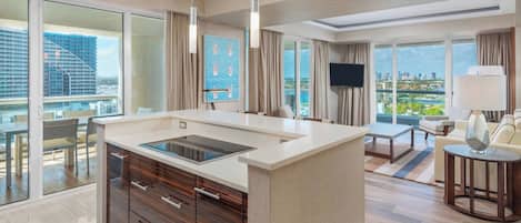 Una habitación de hotel moderna con una isla de cocina, ventanas amplias, un televisor de pantalla plana y vistas a la ciudad.