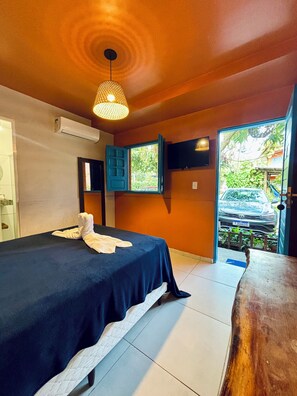 A bedroom with a bed, an air conditioner, a TV, a window with blue shutters, and a view of a car outside. - Brisa do Porto Pousada (Ipojuca)